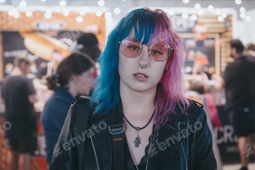 Preview: Portrait of a young female with blue and pink hair wearing sunglasses with a blurred background