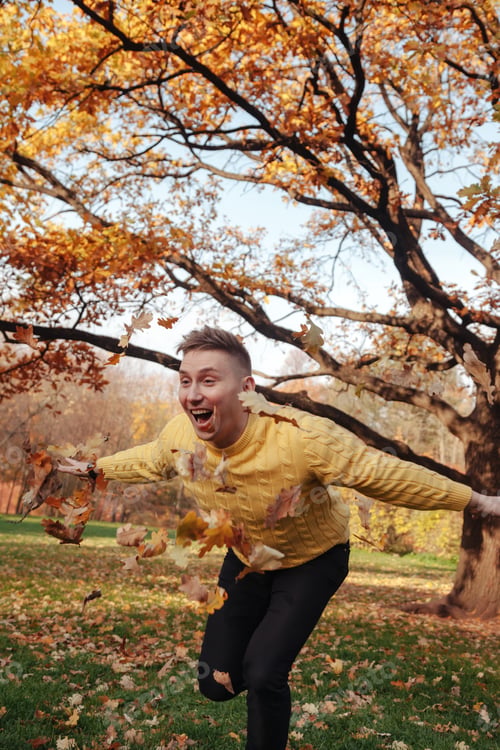 Preview: Happy guy throwing fall leaves in autumn park, joyful outdoors, arms outstretched