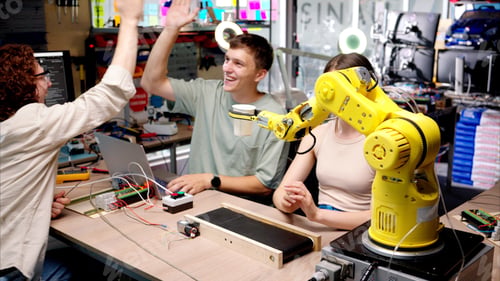 Preview: Three young happy engineers fixing an yellow robotic arm in the workshop, computer programming