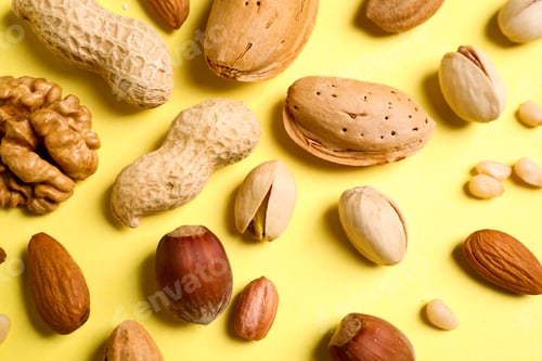 Preview: Different delicious nuts on yellow background, flat lay