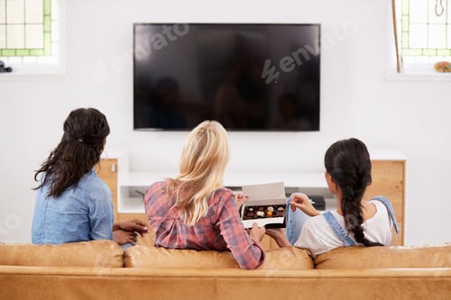 Preview: Female Friends Sitting On Sofa Watching Television Eating Candy