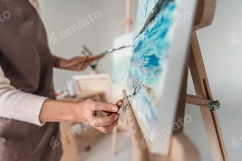 Preview: selective focus of artist with art tools drawing on easel