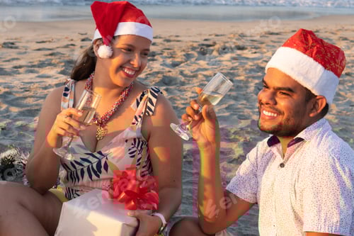 Preview: Happy couple celebrating christmas on the beach with champagne and gifts