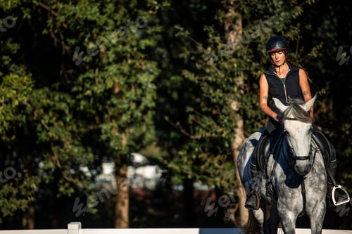 Preview: copyspace Young woman rider training with her horse at the ranch with green trees in the background