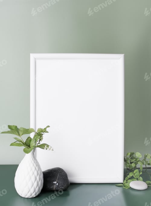 Preview: biophilic design. White blank frame and stones and plants in a vase. green background.