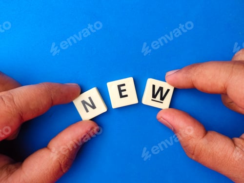 Preview: Top view hand holding toys letters with the word NEW on blue background.