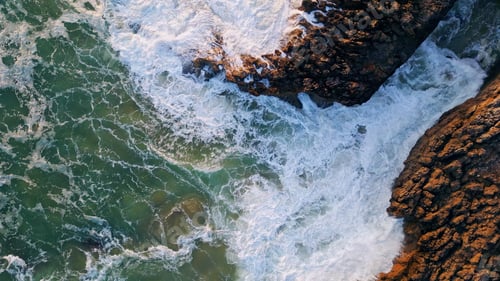 Preview: Rough sea waves washing seashore stones. Top drone view ocean crashing on rocks