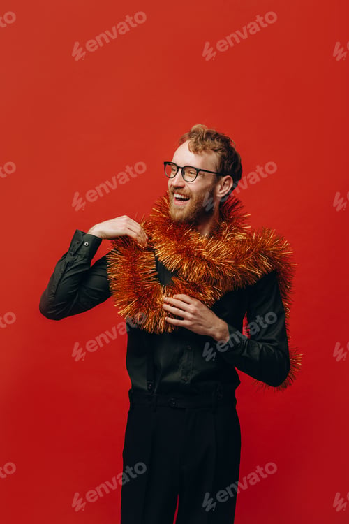 Preview: Red-haired cheerful man in glasses and golden boa at New Year party with confetti. Studio photo.