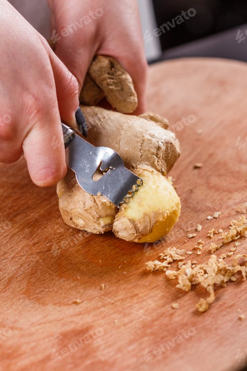 Preview: young woman in a gray apron peeling a ginger root