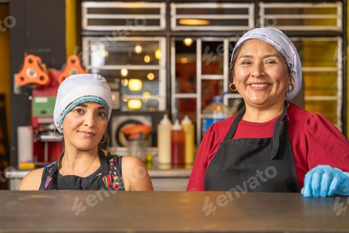 Preview: Two happy cooks smiling behind counter in a fast food restaurant kitchen