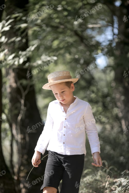 Preview: Portrait of the blode hair boy in straw hat with blurred summer greenery background