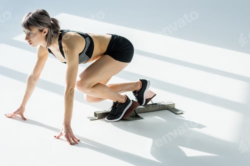 Preview: side view of sporty woman in starting position on grey