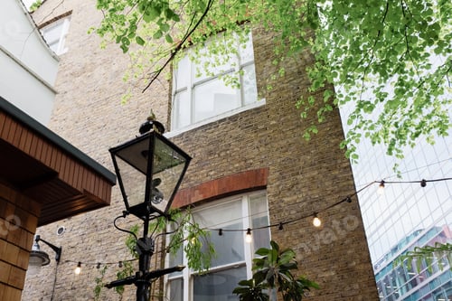 Preview: Street lamp illuminating brick building with green leaves and string lights