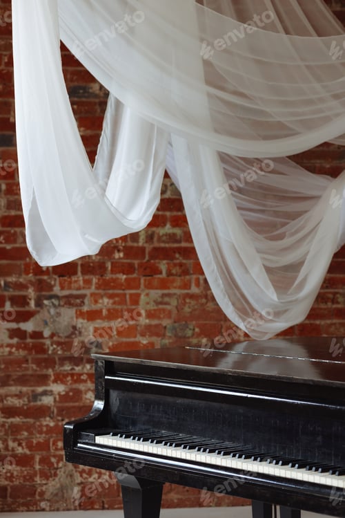 Preview: Old black grand piano in loft room with red brick wall and white fabric drapes