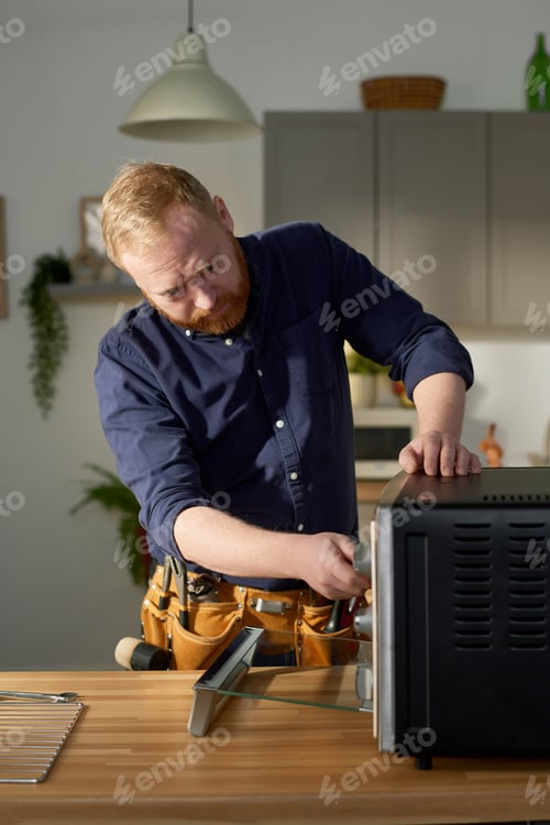 Preview: Man Fixing Oven Appliance In Light Filled Kitchen