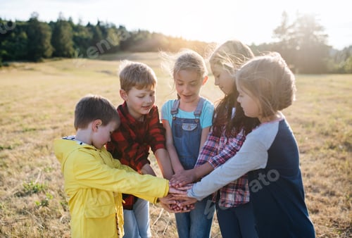 Preview: Group of school children standing on field trip in nature, putting hands together