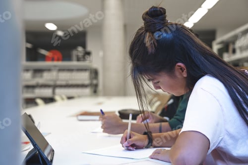 Preview: Focused woman writing on paper in library
