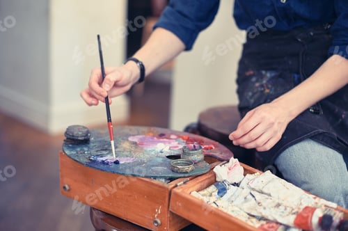 Preview: Young Woman Artist Working On Painting In Studio. Selective focus on foreground.