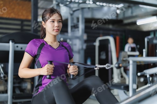 Preview: Asian woman doing seated cable rows exercise in gym for back workout