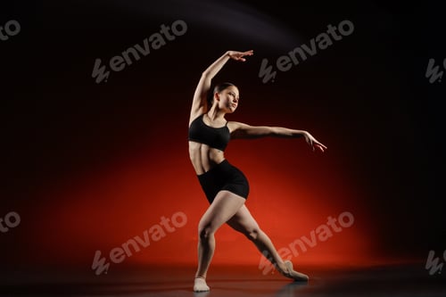 Preview: Young woman dancer stretching in studio on red background with copy space