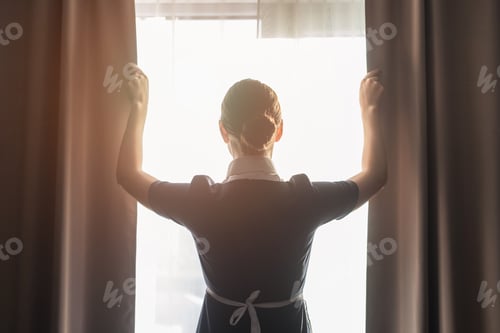Preview: back view of maid adjusting curtains in hotel room