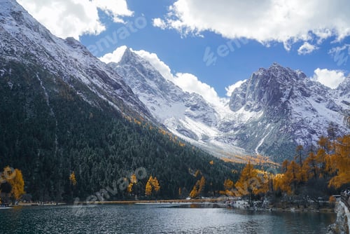 Preview: Snowy mountain peak with autumn forest and calm lake under cloudy blue sky