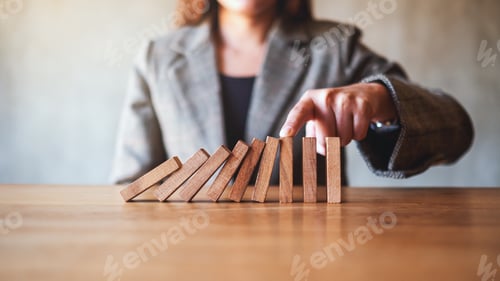 Preview: a businesswoman try to use finger to stop falling wooden dominoes blocks