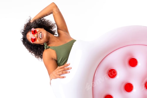 Preview: Pretty african female lies in swimsuit with rubber beach mattress and smiles isolated on white