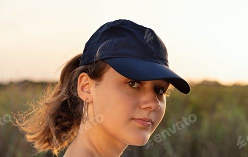 Preview: Teen girl in dark blue baseball cap at sunset