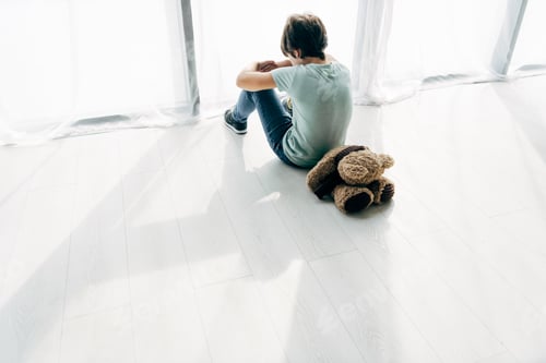 Preview: high angle view of kid with dyslexia sitting on floor with teddy bear