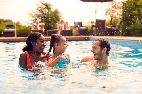 Preview: Smiling Mixed Race Family On Summer Holiday Having Fun Splashing In Outdoor Swimming Pool