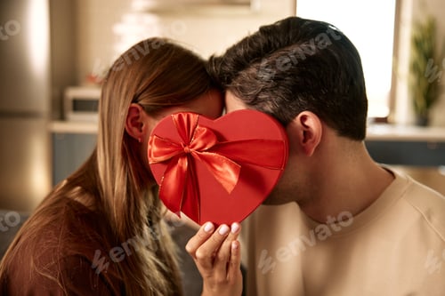 Preview: Couple hiding behind heart shaped gift box on Valentine's Day