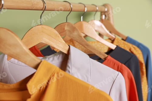 Preview: Collection of trendy women's garments on rack near green wall, closeup. Clothing rental service