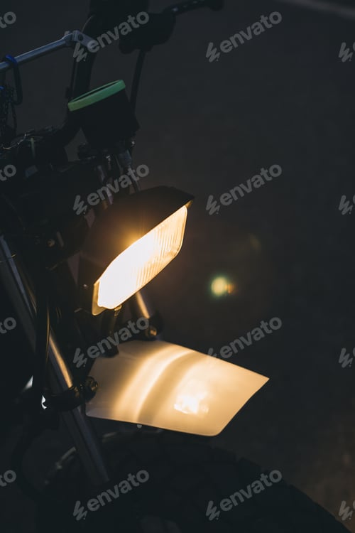 Preview: A close-up of a stylish cafe racer with the headlights on at dusk.