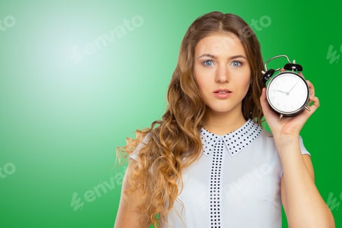 Preview: Woman holds alarm clock with surprise on her face in front of green background