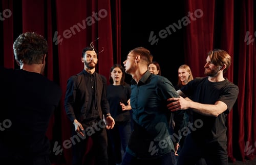 Preview: Working together. Group of actors in dark colored clothes on rehearsal in the theater