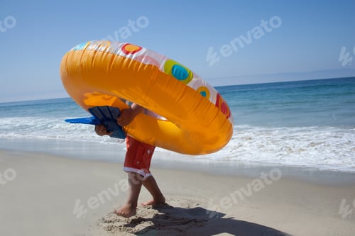Preview: Young boy carrying rubber ring on beach