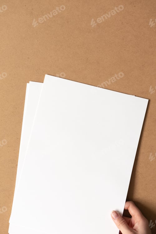 Preview: Hand hold white empty clean paper sheets on cardboard background. Top view, vertical