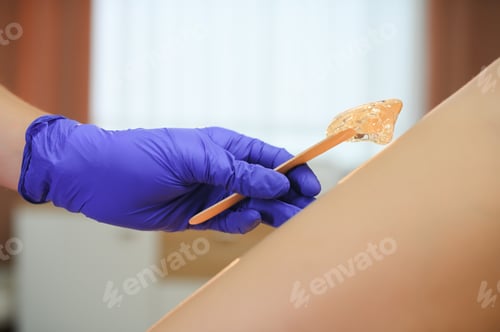 Preview: Woman having hair removal procedure on leg with sugaring paste in salon
