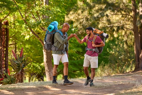 Preview: Two Male Friends With Backpacks Fist Bumping On Vacation Hiking Through Countryside Together