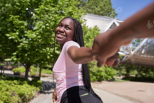 Preview: happy young african american woman holding hand of his girlfriend while walking by a park.