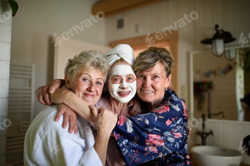 Preview: Happy senior women friends in bathrobes having fun indoors at home, looking at camera