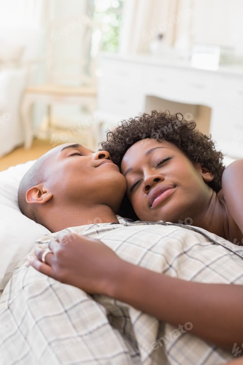 Preview: Happy couple lying in bed together at home in the bedroom