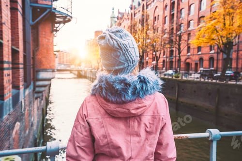 Preview: Back view of adult woman tourist enjoying autumn beautiful sunset scene of Speicherstadt historic