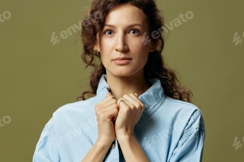 Preview: Serious adorable curly beautiful female in jeans casual shirt touches collar looks at camera posing