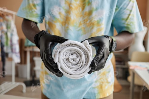 Preview: Hands of young craftsman in protective gloves holding rolled t-shirt