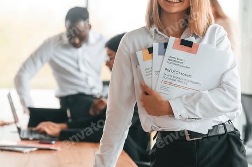 Preview: Project manager is standing with documents. Group of office workers are together indoors
