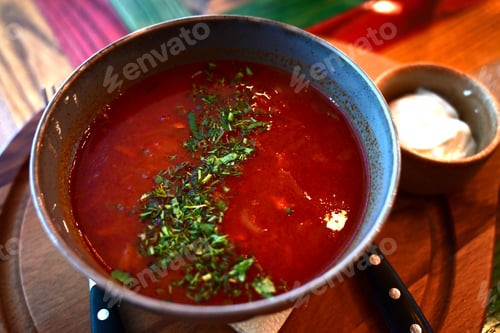 Preview: Russian traditional dish borscht with herbs and sour cream in a semicircular plate on a wooden board