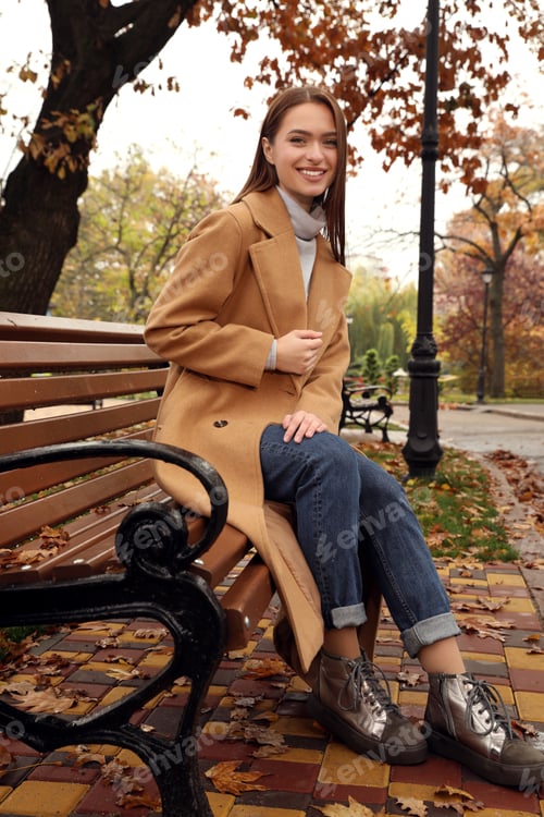 Preview: Beautiful young woman wearing stylish clothes on bench in autumn park