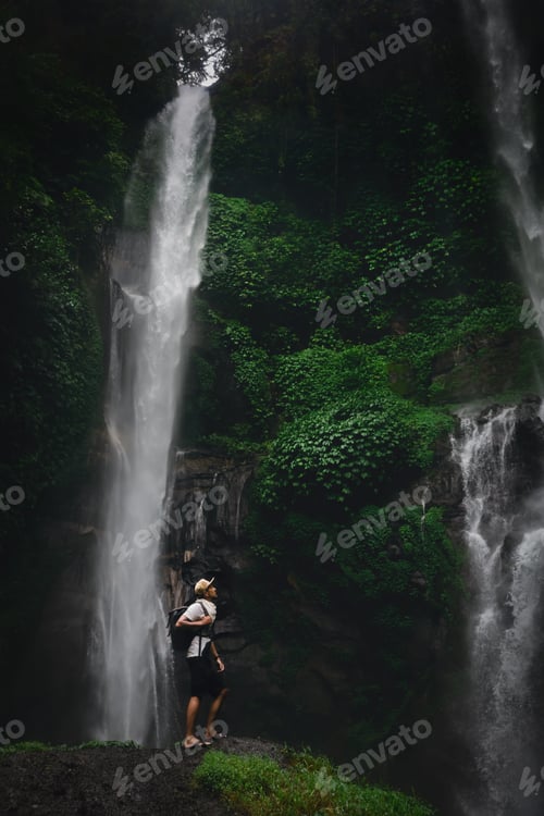 Preview: Happy man backpacker enjoying amazing tropical waterfall on background nature landscape. Travel